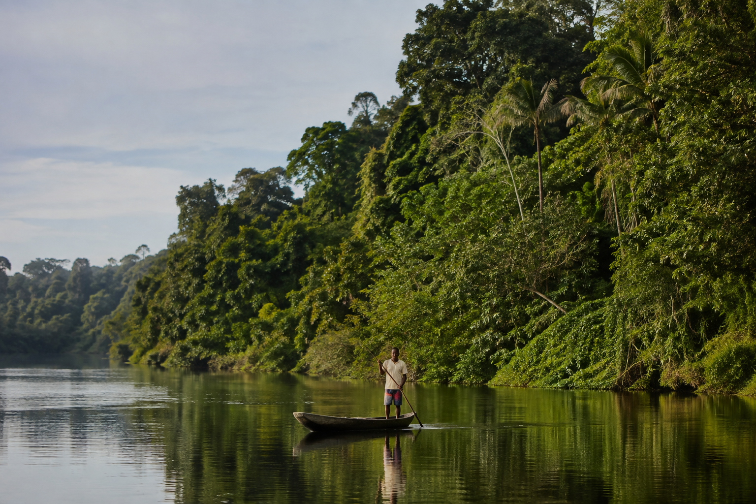 Pessoa negra em uma canoa diante de um rio e uma floresta preservada